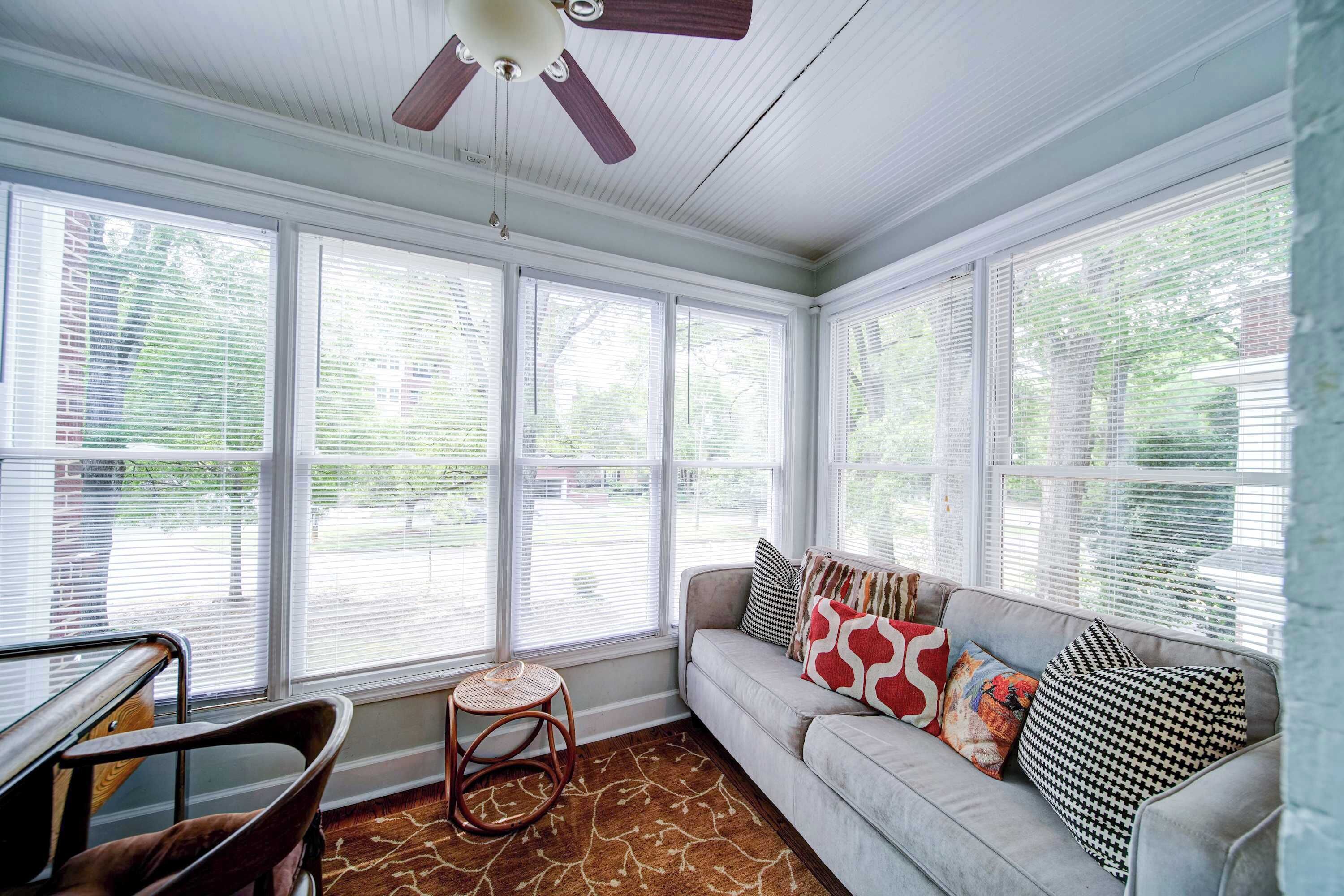 A sunroom with a ceiling fan, a cushioned seating area, and large windows.