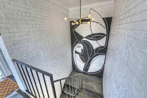 Een trap met een witte bakstenen muur, een zwart-wit abstracte muurschildering en een moderne lamp.