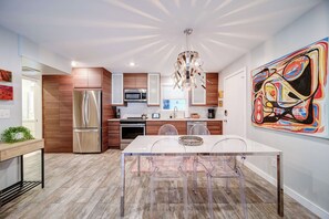 A modern kitchen with a stainless steel refrigerator, microwave, and oven, a dining table with transparent chairs, and a colorful abstract painting on the wall. - Cozy One-Bedroom Apartment in Myers Park (Charlotte)
