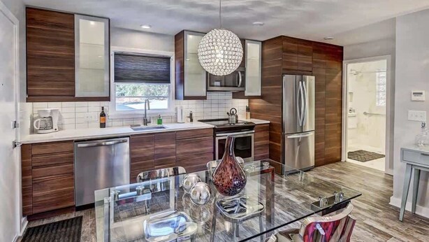 A modern kitchen with wooden cabinets, stainless steel appliances, and a glass dining table.