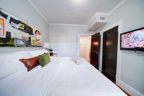 Ein Schlafzimmer mit einem Bett, einem an der Wand befestigten Fernseher und einer Tür zu einem weiteren Raum.