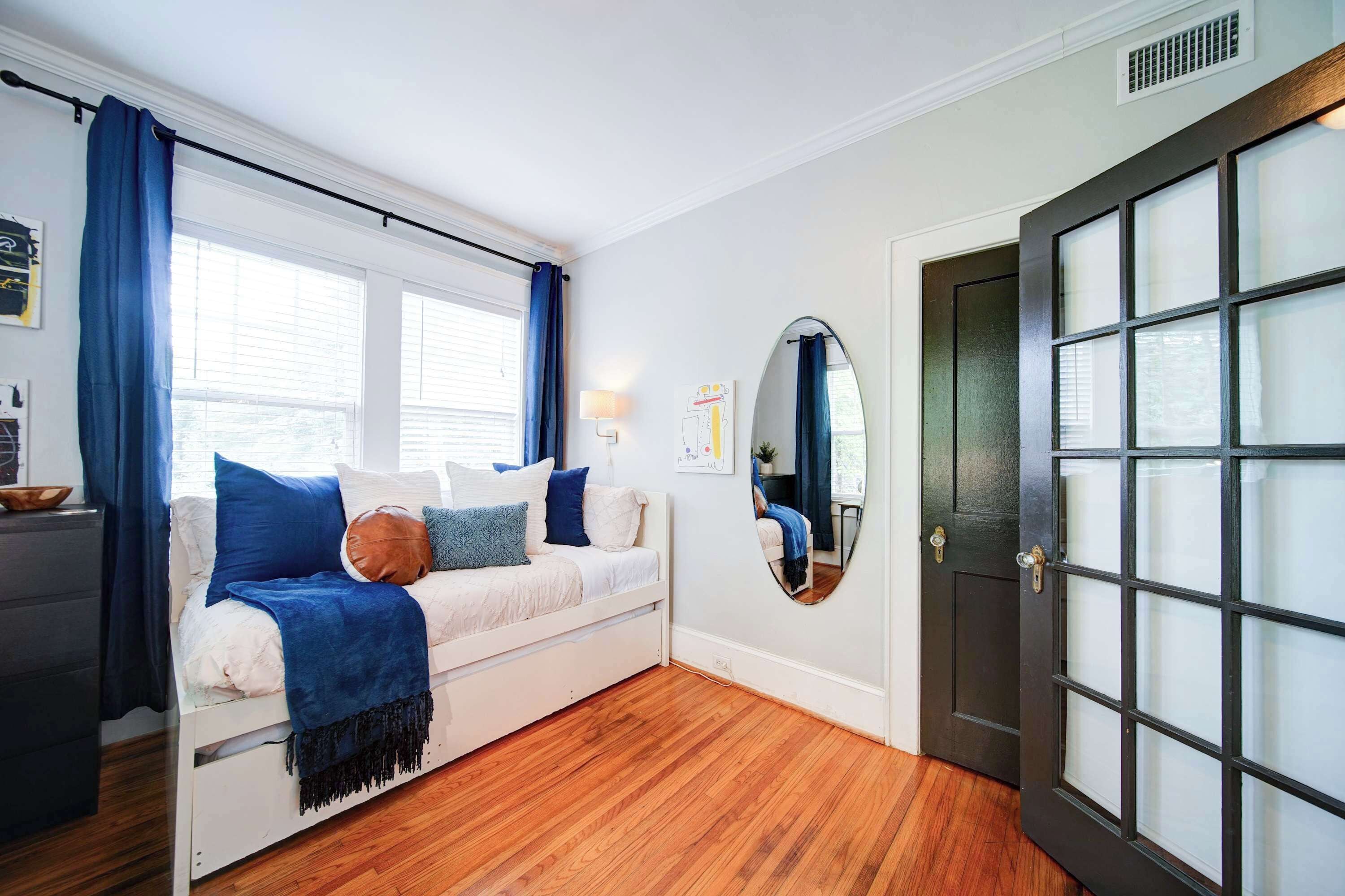 A bedroom with a white bed, blue curtains, a wooden floor, and a dark door with glass panels.