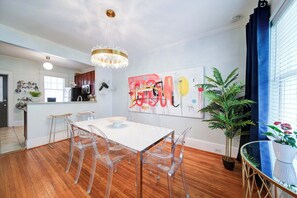 A modern kitchen with a dining area, wooden flooring, and a chandelier.