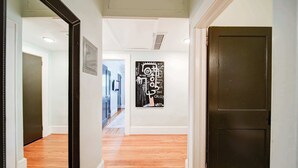 Un pasillo con piso de madera, una puerta oscura y una obra de arte colgada en la pared.