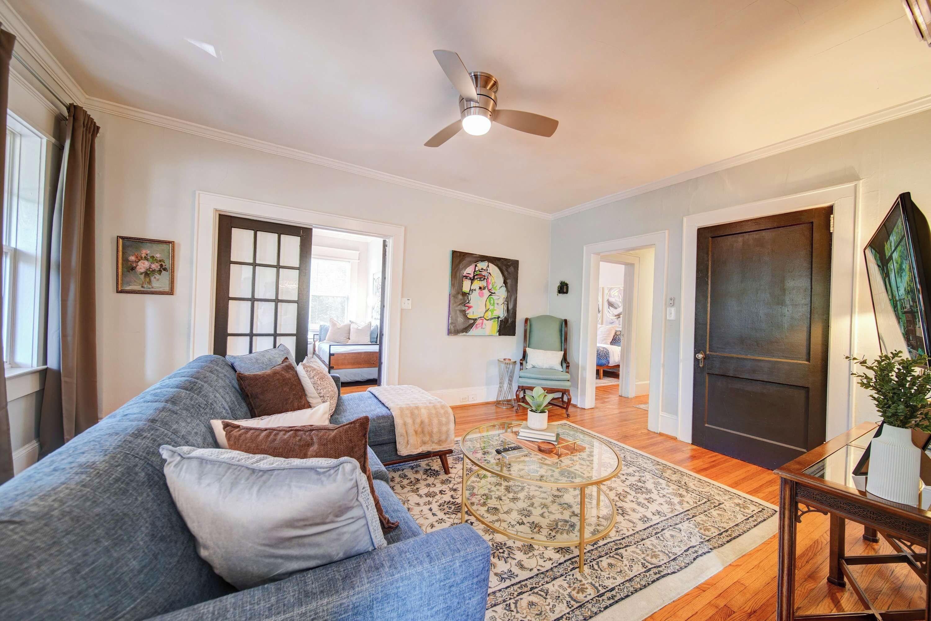A spacious living room with a blue sofa, a glass coffee table, and a ceiling fan.