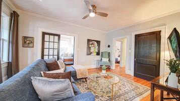 A spacious living room with a blue sofa, a glass coffee table, and a ceiling fan.