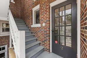 A brick building with a dark door, a window, and a staircase. - The Home Collection: Historic 2BR Ground Floor Condo Steps to Latta Park (Charlotte)