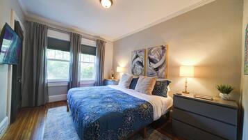 A bedroom with a large bed, two bedside tables, a nightstand, a TV, and a window with curtains.