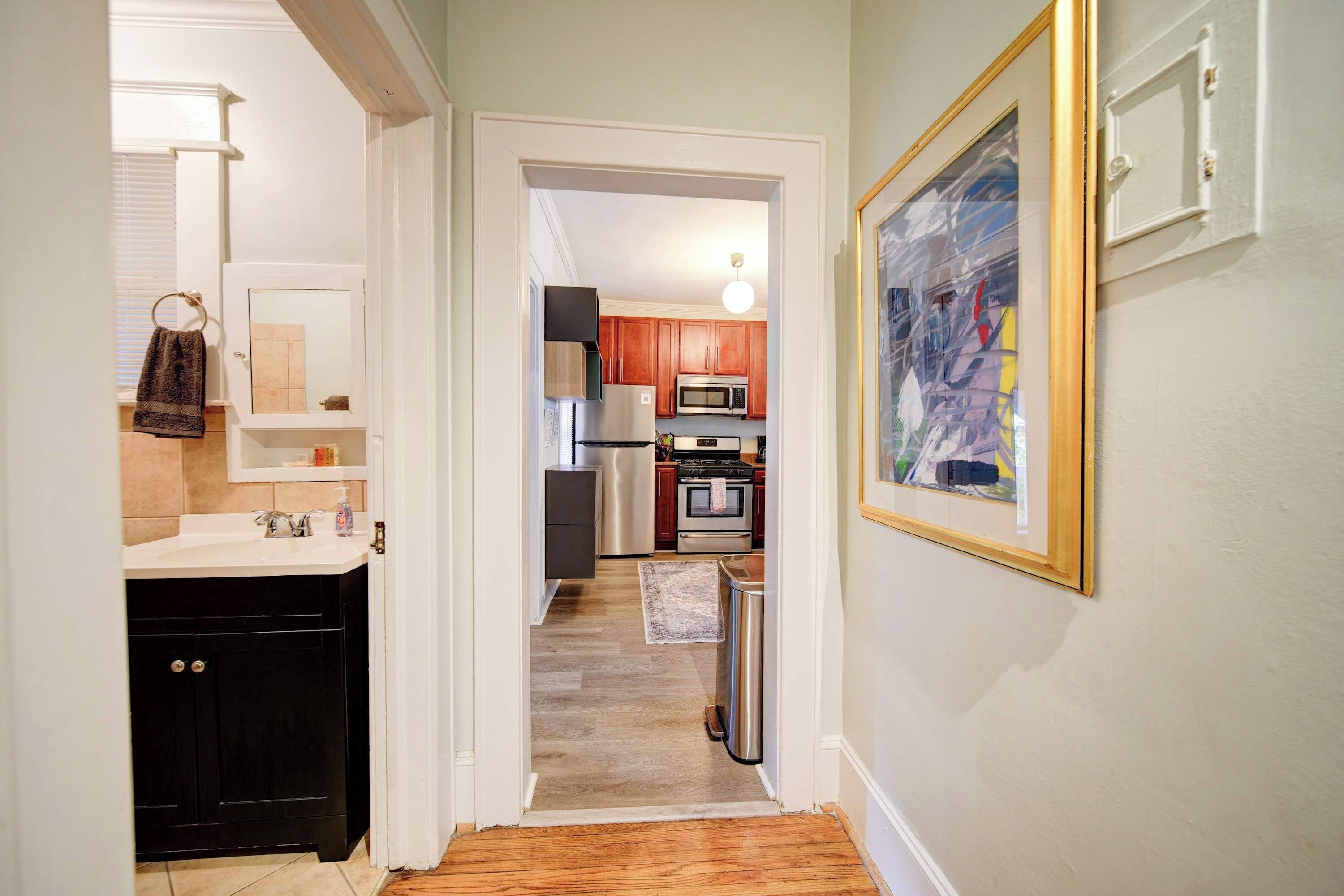 A hallway leading to a kitchen with wooden cabinets, a stainless steel refrigerator, and a microwave.