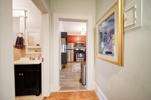 Un pasillo que conduce a una cocina con armarios de madera, un refrigerador de acero inoxidable y un microondas.