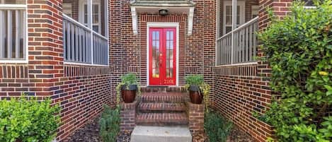 Un edificio de ladrillo con puerta roja, un pequeño porche y escalones que conducen a la entrada.