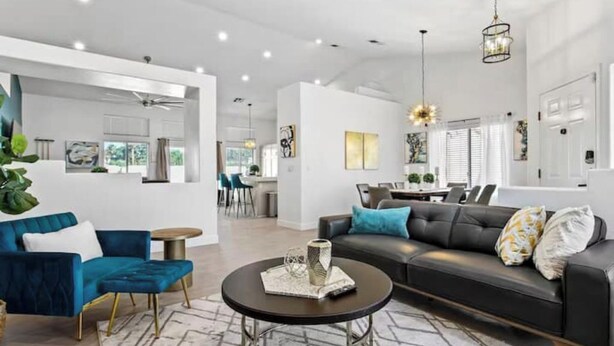 A modern living room with a dark sofa, blue armchair, and a round coffee table. - Stunning 5BD Escape w/ Billiard Room & Pool! (North Las Vegas)