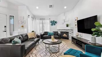 A modern living room with a black leather sofa, a round coffee table, and a flat-screen TV mounted on the wall.