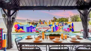 An outdoor dining area with a pool, a mural of Las Vegas, and a covered seating area.