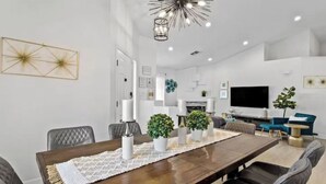 A modern dining area with a long wooden table, cushioned chairs, and decorative plants. - Stunning 5BD Escape w/ Billiard Room & Pool! (North Las Vegas)