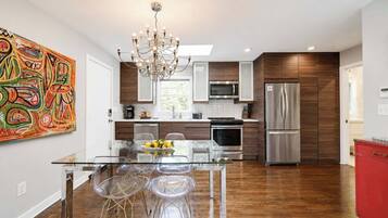 A modern kitchen with a glass dining table, stainless steel appliances, and a chandelier.