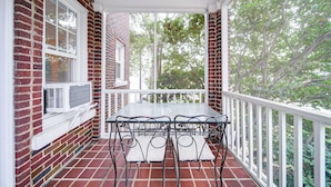 Une terrasse couverte avec une façade en briques, une balustrade blanche et une table avec des chaises.