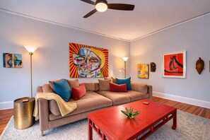 Una sala de estar con un sofá color beige, una mesa de centro roja y varias obras de arte en las paredes.