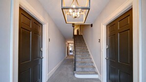 A hallway with carpeted stairs, dark doors, and a geometric light fixture.