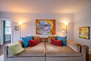 Una sala de estar con un sofá color crema, cojines de colores y dos lámparas fijadas a la pared.
