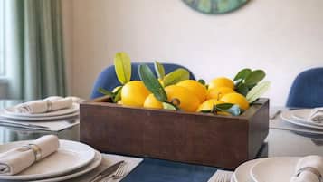 Une table à manger dressée avec des assiettes, des couverts et un saladier en bois rempli de citrons et de feuilles.