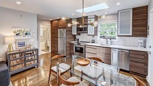 Een moderne keuken met een glazen eettafel, houten stoelen en roestvrijstalen apparatuur.