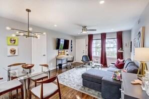 A modern living room with a glass dining table, a gray sofa, and a ceiling fan.