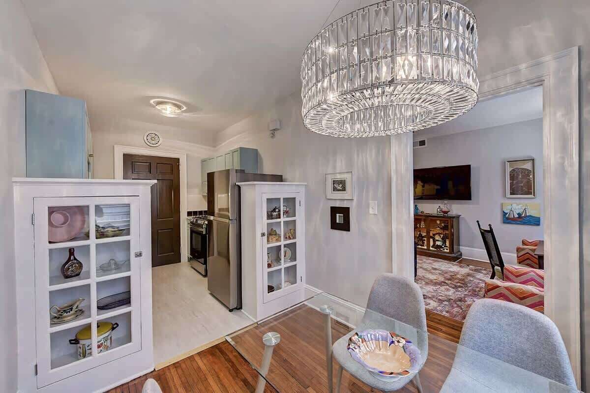 A modern kitchen with white cabinetry, a stainless steel refrigerator, and a chandelier.