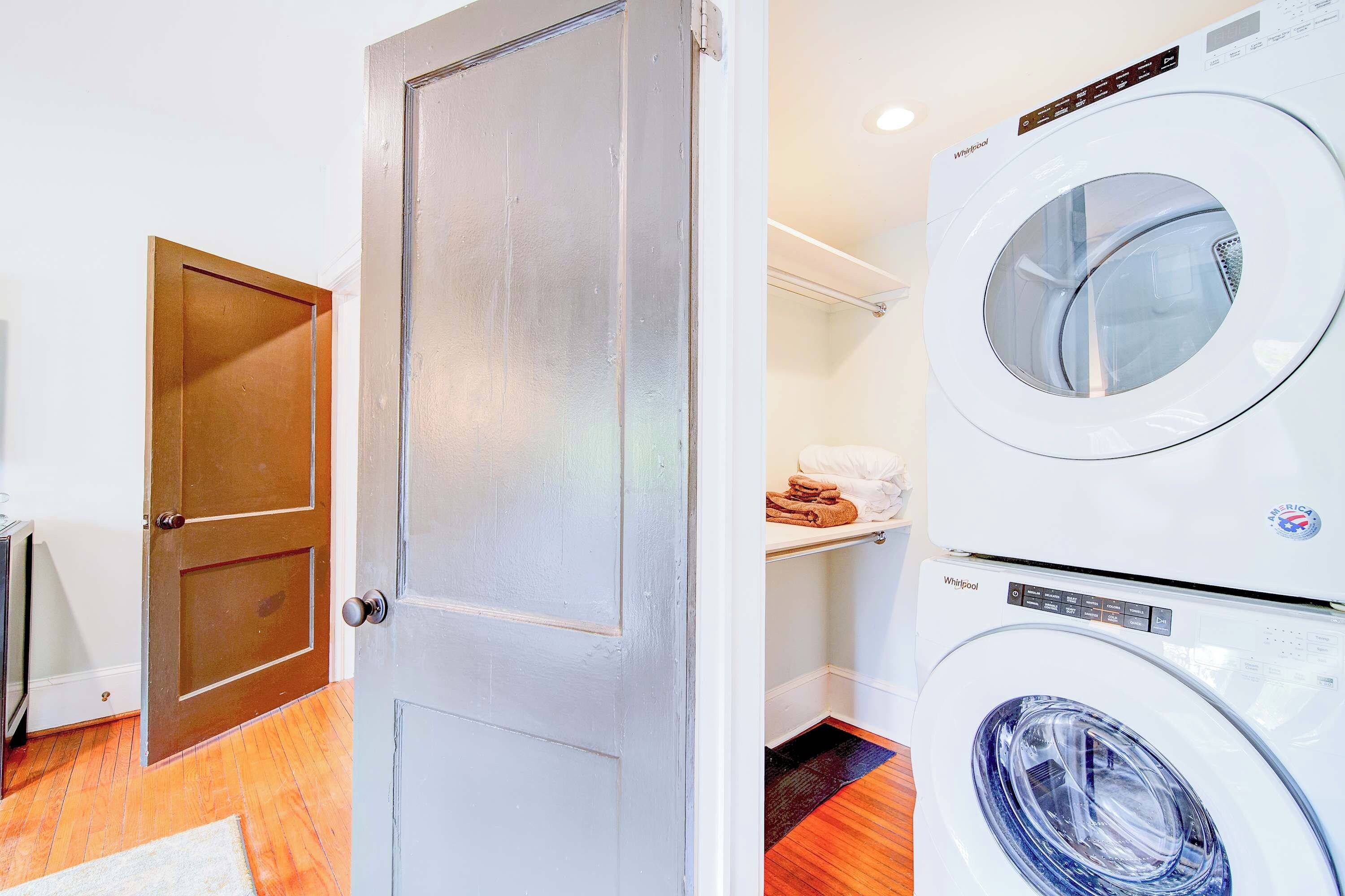 A laundry room with a front-loading washer and dryer, a wooden door, and a shelf with folded towels.