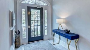 A hallway with a dark blue door, a white wall, a blue console table with a lamp, and a patterned rug.