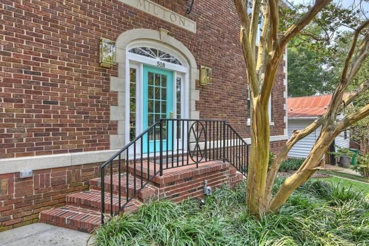 A brick building with a turquoise door and a black metal staircase leading to the entrance.