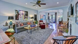 A spacious living room with a ceiling fan, a large painting, and a dining area in the background. - The Home Collection: Historic Myers Park 2BR · Near Atrium Health (Charlotte)