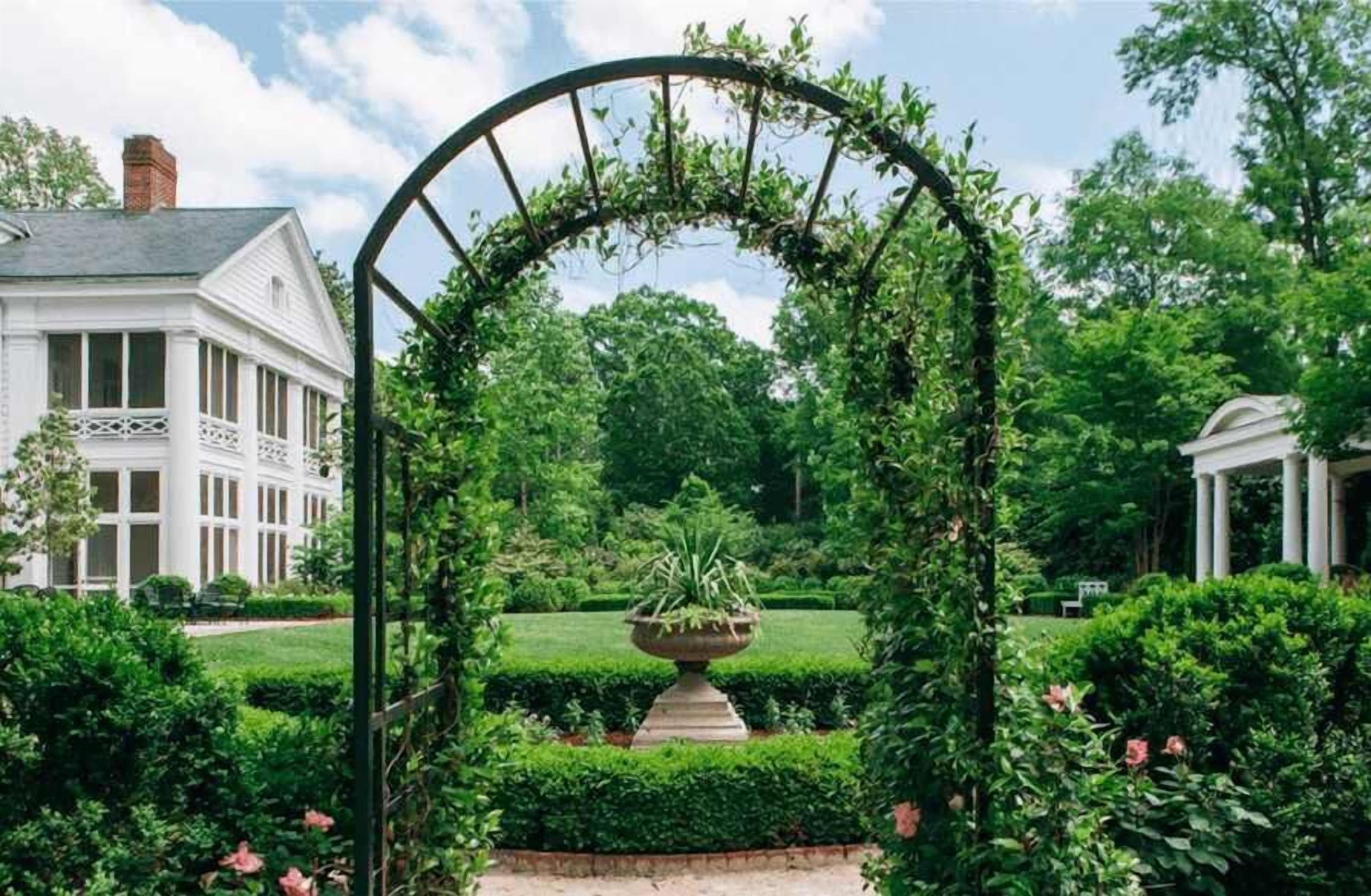 A garden with a white building, a pergola, and a fountain.
