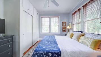 Een slaapkamer met een bed, een dressoir, een plafondventilator en een raam met jaloezieën.