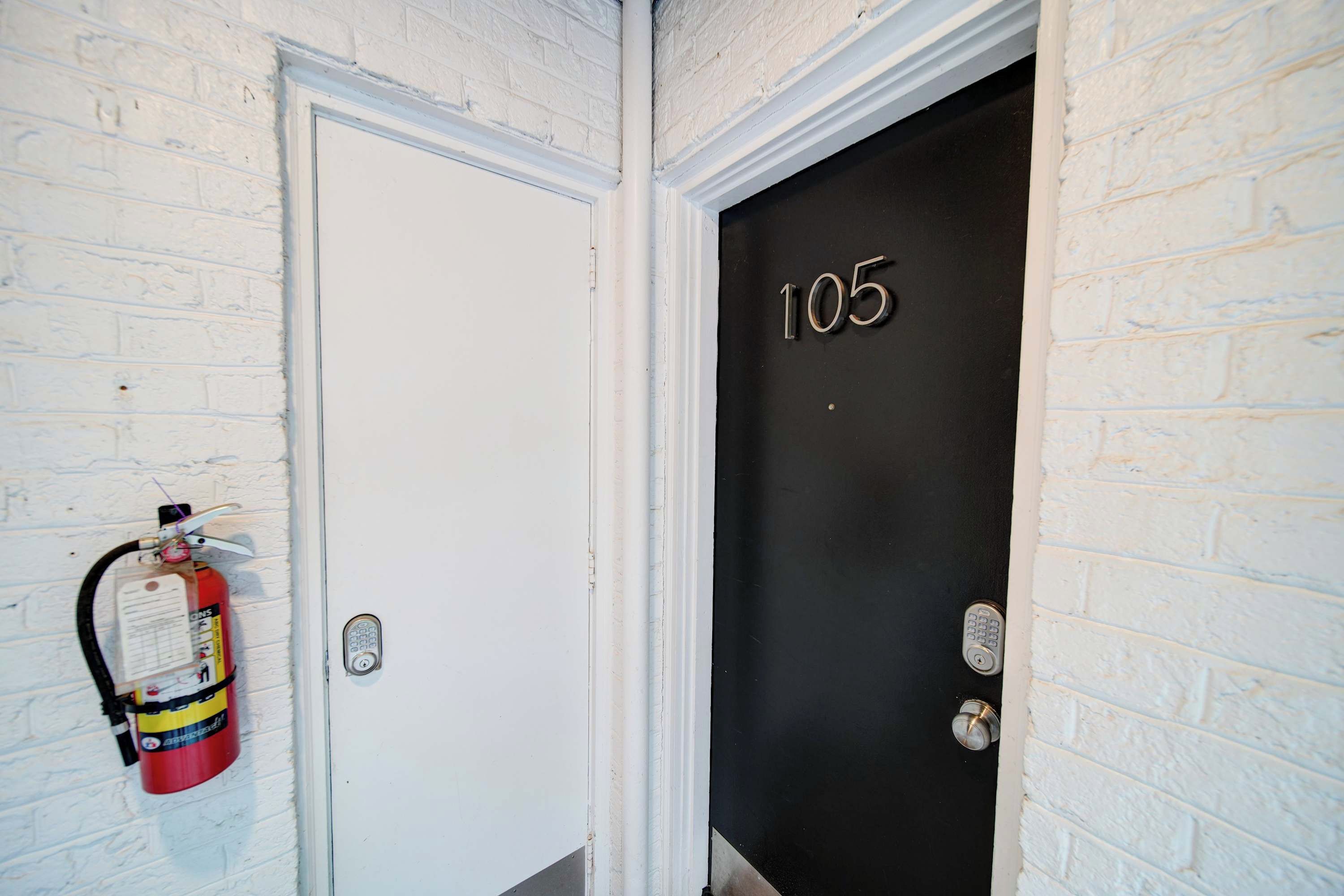 A white door with a black door number '105' and a fire extinguisher mounted on the wall beside it.