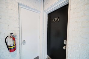 Une porte blanche avec un numéro de porte noir, le « 105 », et un extincteur fixé au mur à côté.
