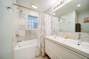 A modern bathroom with a bathtub, a shower with a glass door, a large mirror, and a vanity with a sink and multiple bottles.