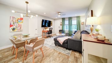 A modern living room with a glass dining table, comfortable seating, a flat-screen TV, and a cozy sofa.