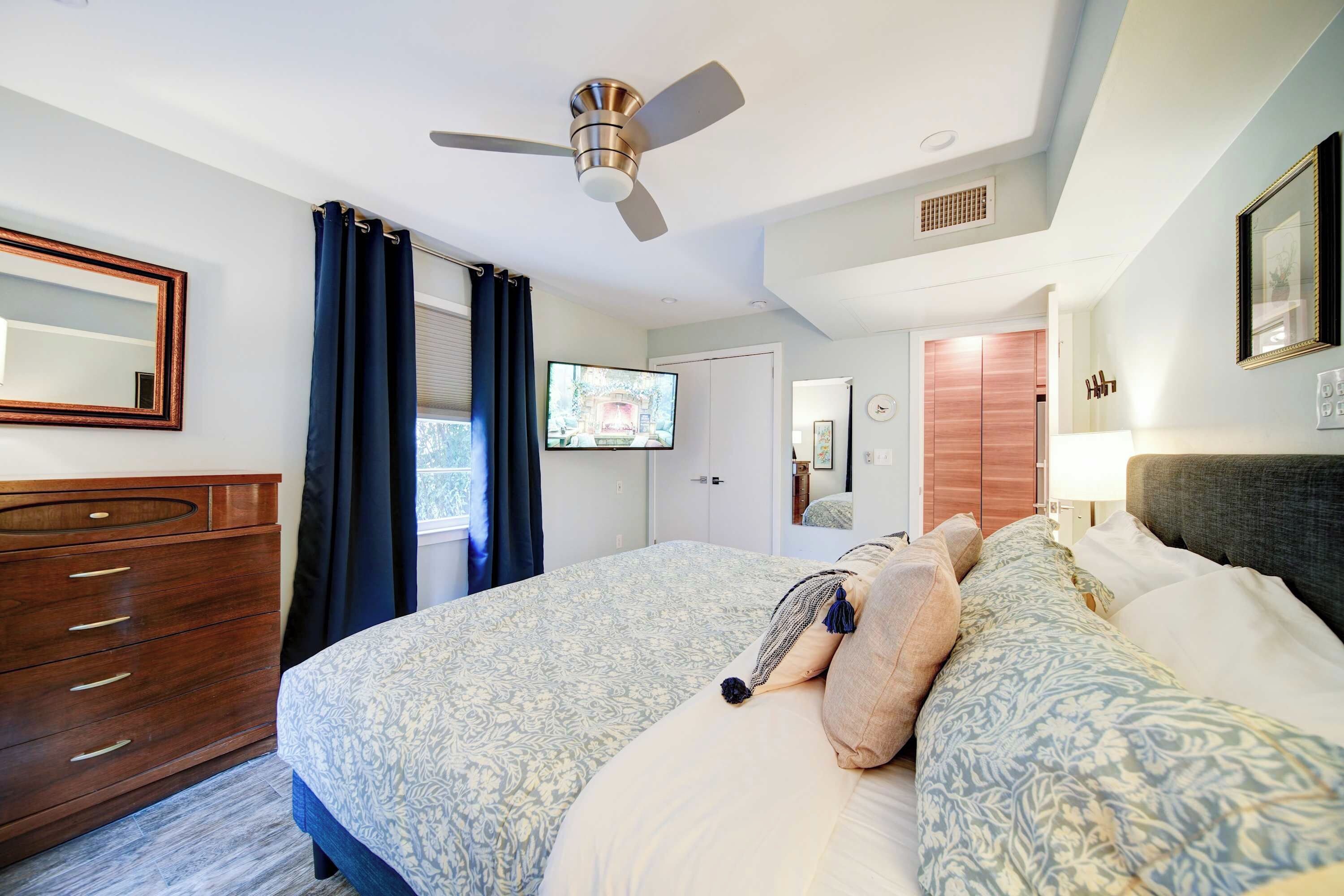 Un dormitorio con cama, cómoda, ventilador de techo, televisión y una puerta que da a otra habitación.