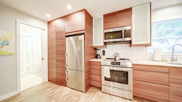 A modern kitchen with stainless steel appliances, wooden cabinetry, and a tiled backsplash.