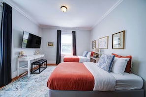 A hotel room with two beds, a desk, a television, and artwork on the walls.