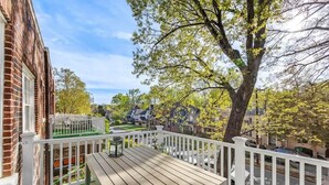 A wooden deck with a table and chairs, surrounded by a white fence, overlooking a residential neighborhood with houses and trees.