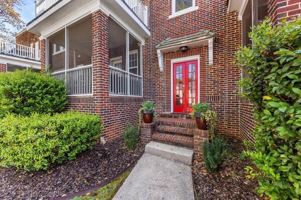 A two-story brick building with a red door and a covered porch.