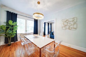A dining area with a white table, clear chairs, a chandelier, and a potted plant. - Boutique 2BR Dilworth Condo | Near Atrium and Novant Health (Charlotte)