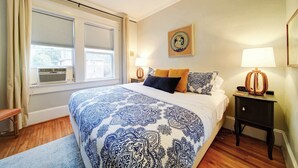 Une chambre à coucher avec un grand lit, une table de chevet avec une lampe et une fenêtre avec des stores.