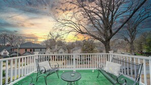 Une terrasse couverte, aménagée avec du mobilier d’extérieur, une clôture blanche et une vue sur des maisons et des arbres.