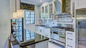 Une cuisine moderne avec des armoires blanches, une cuisinière en acier inoxydable et une grande fenêtre.