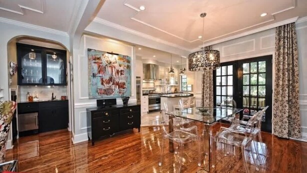 A spacious kitchen with a glass dining table and chairs, a large painting on the wall, and a chandelier.