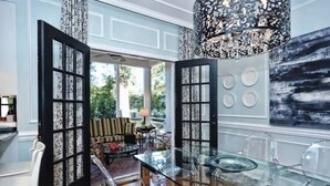A modern kitchen with a glass dining table, a black and white patterned door, and a large abstract painting on the wall.