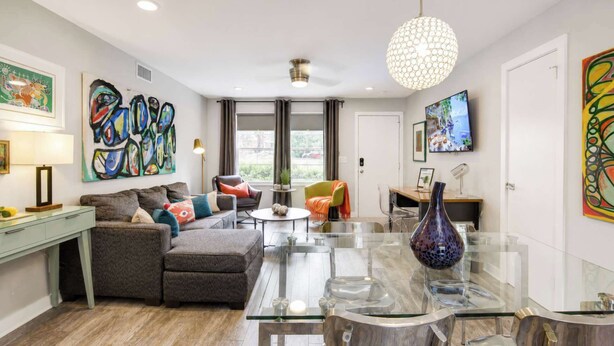 A modern living room with a glass dining table, a sofa, a coffee table, and a TV. - Modern Myers Park 1BR · Ground Floor · Free Parking near Atrium CMC & Uptown (Charlotte)